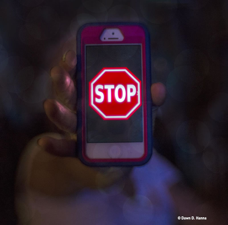 A hand holding to the camera a smartphone with a stop sign on the screen--looks graphic cartoon like